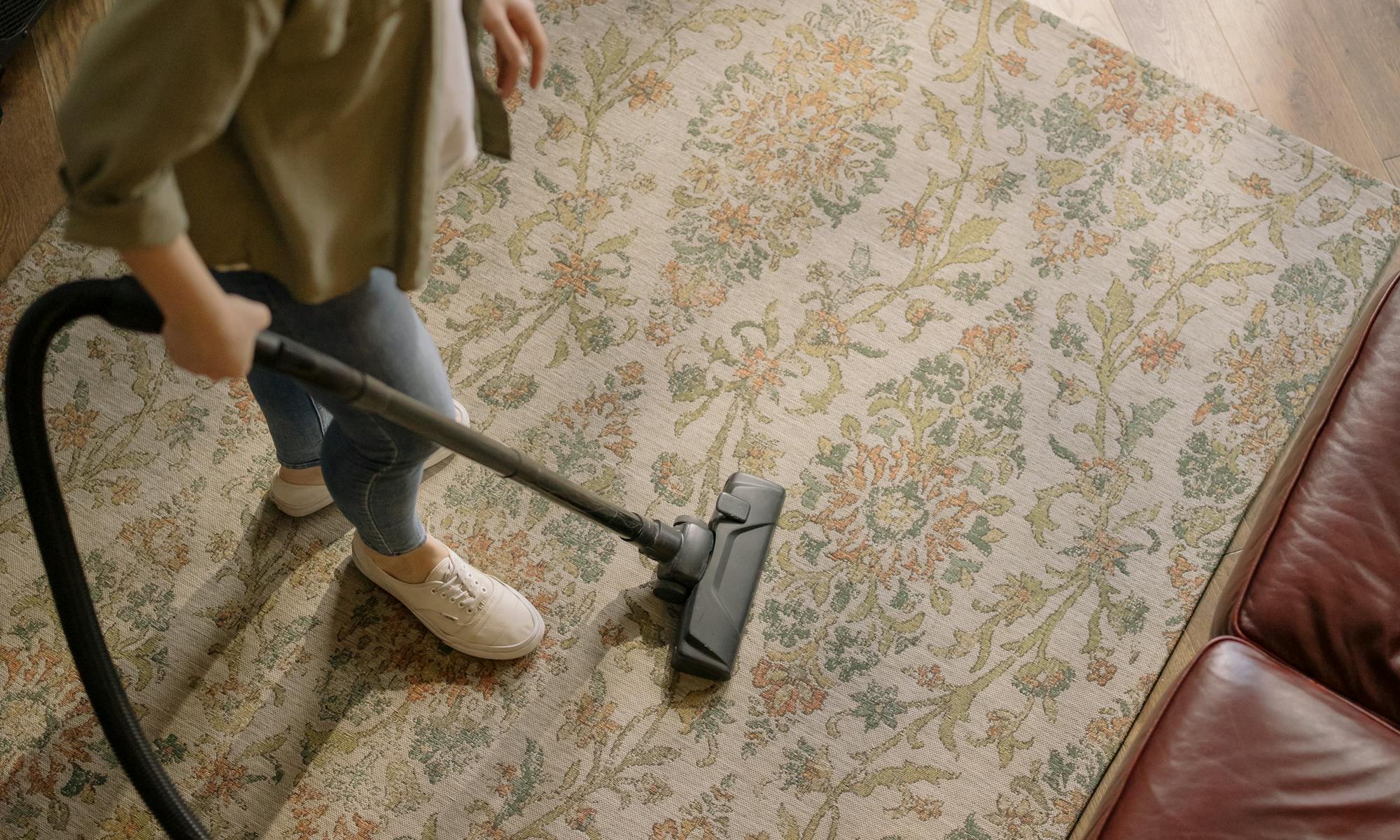 Overhead view of a woman vacuuming a carpet at home, highlighting cleanliness and housekeeping.